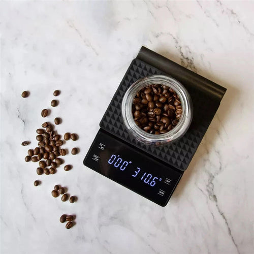 Black digital coffee scale with LED display weighing a jar of coffee beans on marble countertop